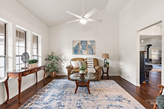 living area with lofted ceiling, wood finished floors, a ceiling fan, baseboards, and a wood stove