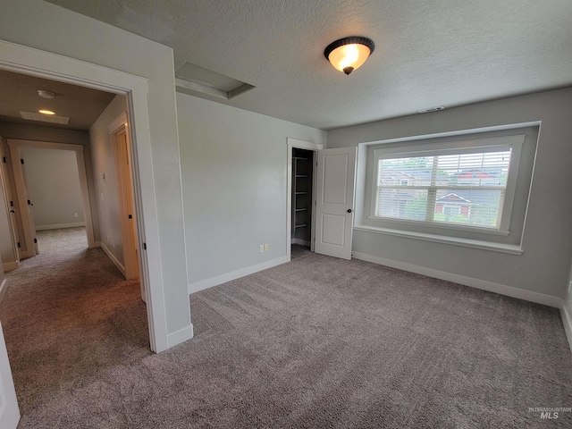 unfurnished bedroom featuring attic access, baseboards, a textured ceiling, and carpet