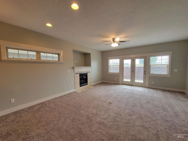 unfurnished living room featuring a tiled fireplace, baseboards, ceiling fan, and light colored carpet