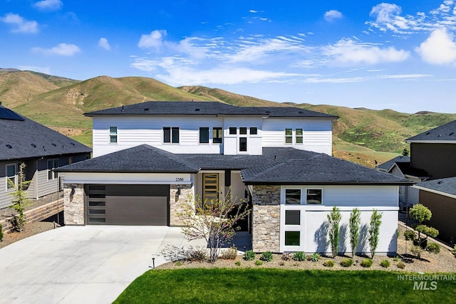 view of front facade with a mountain view, concrete driveway, roof with shingles, stone siding, and a garage