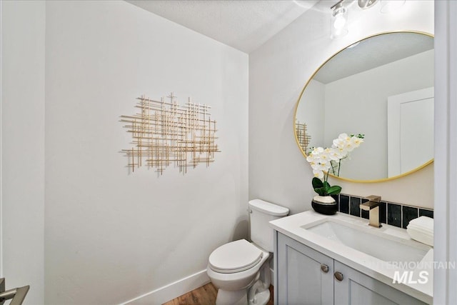 half bath featuring vanity, toilet, wood finished floors, and baseboards