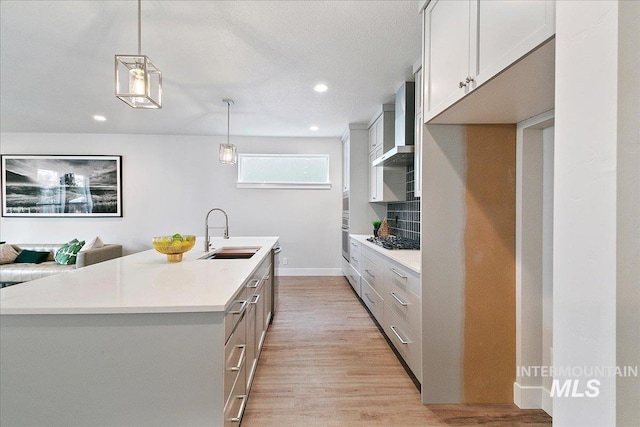 kitchen with light countertops, gas cooktop, wall chimney range hood, and a sink