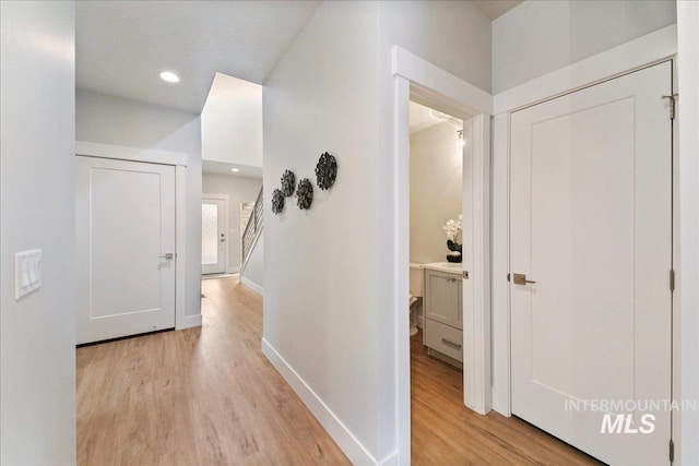 corridor featuring recessed lighting, light wood-type flooring, baseboards, and stairway