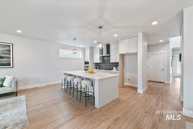 kitchen featuring a breakfast bar, light countertops, an island with sink, and light wood-style floors