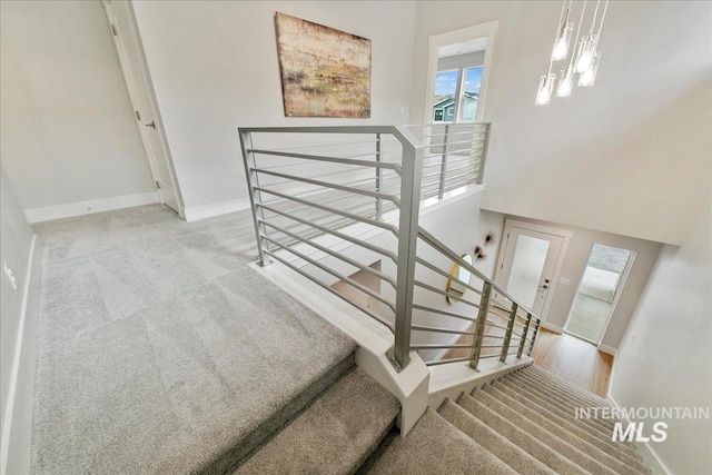 stairs featuring baseboards, a towering ceiling, and carpet flooring