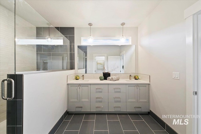 bathroom with double vanity, a shower stall, baseboards, and a sink