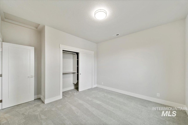 unfurnished bedroom featuring visible vents, a textured ceiling, a closet, baseboards, and light colored carpet