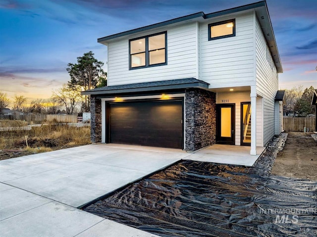 view of front facade featuring a garage, stone siding, concrete driveway, and fence