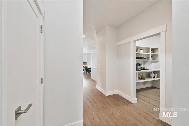 corridor featuring built in features, baseboards, and light wood-style flooring