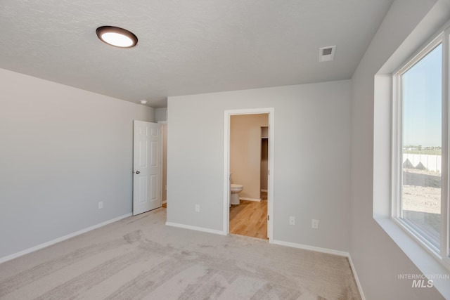 unfurnished bedroom with connected bathroom, light colored carpet, and a textured ceiling