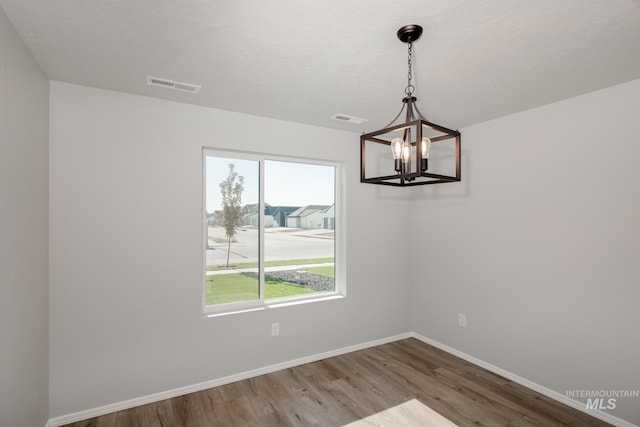 unfurnished dining area featuring hardwood / wood-style floors, a textured ceiling, and an inviting chandelier