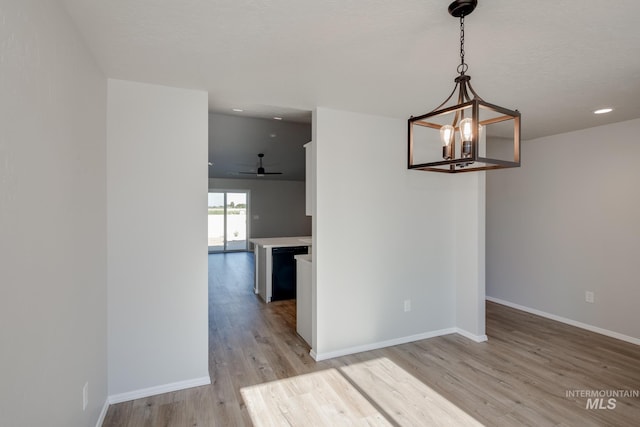 unfurnished dining area featuring ceiling fan with notable chandelier and light wood-type flooring