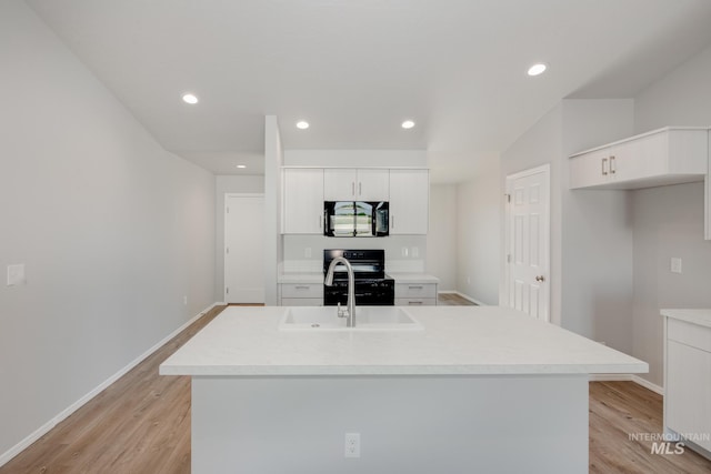 kitchen featuring black appliances, light hardwood / wood-style floors, white cabinets, and a center island with sink