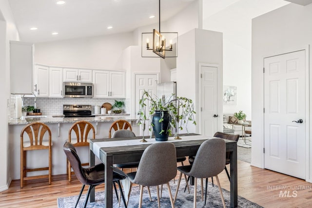 dining area with an inviting chandelier, high vaulted ceiling, and light wood-type flooring