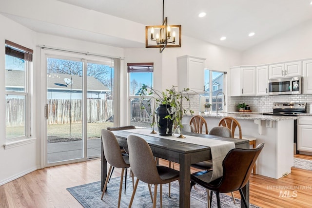 dining area featuring vaulted ceiling, sink, a notable chandelier, and light hardwood / wood-style floors