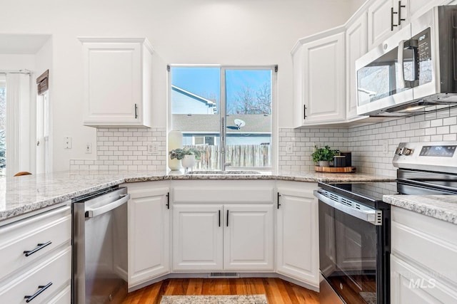 kitchen with sink, light hardwood / wood-style flooring, white cabinets, stainless steel appliances, and backsplash