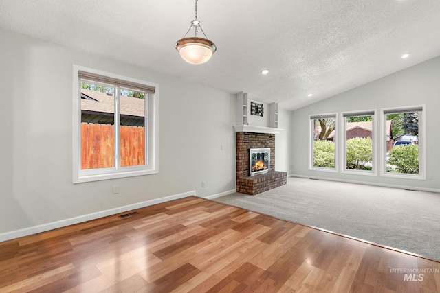unfurnished living room with a textured ceiling, visible vents, a brick fireplace, wood finished floors, and baseboards
