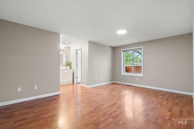 unfurnished room featuring light wood-style floors, a textured ceiling, and baseboards