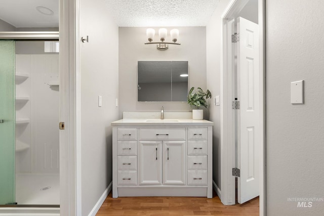 bathroom with vanity, wood finished floors, baseboards, a textured ceiling, and a shower stall