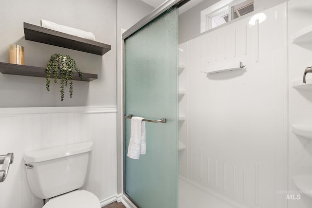 full bath featuring wainscoting, toilet, and a shower stall