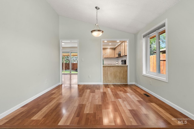 unfurnished dining area featuring vaulted ceiling, plenty of natural light, light wood-style flooring, and visible vents