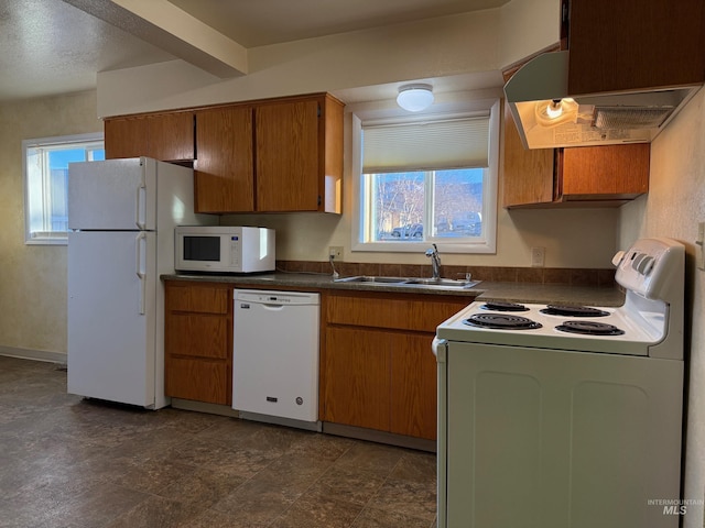 kitchen featuring white appliances, a sink, exhaust hood, brown cabinetry, and dark countertops