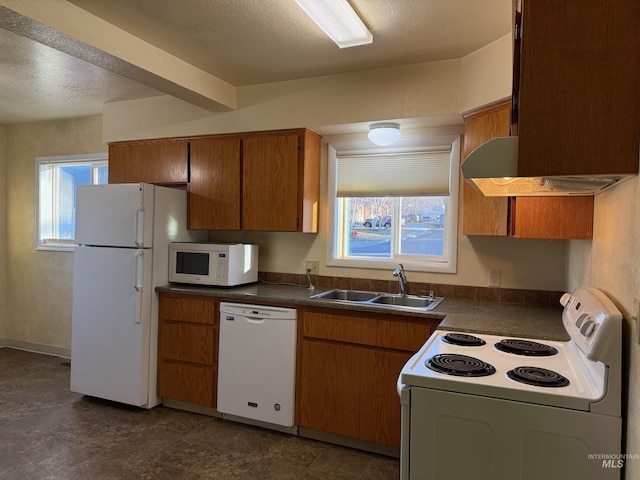 kitchen with white appliances, dark countertops, brown cabinets, a textured ceiling, and a sink