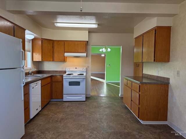 kitchen featuring white appliances, brown cabinetry, dark countertops, under cabinet range hood, and a sink