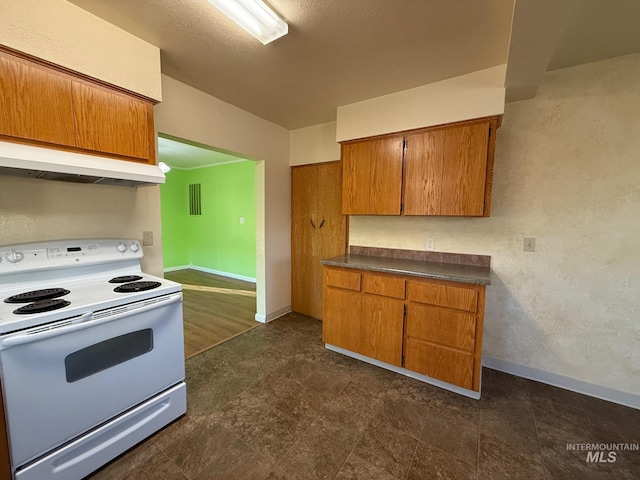 kitchen with dark countertops, under cabinet range hood, brown cabinetry, and white range with electric cooktop