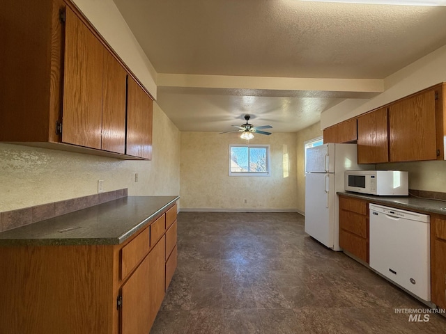 kitchen featuring white appliances, baseboards, brown cabinetry, dark countertops, and a textured ceiling