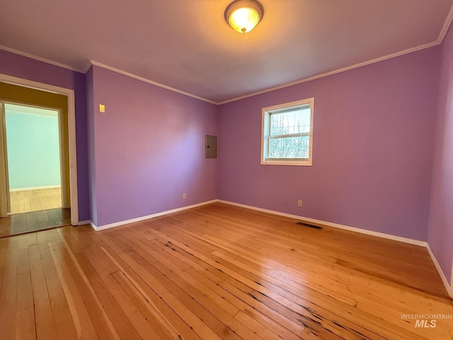 spare room with electric panel, baseboards, visible vents, ornamental molding, and light wood-style floors