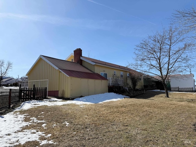 view of snow covered exterior with a lawn, a chimney, a pole building, fence, and an outdoor structure