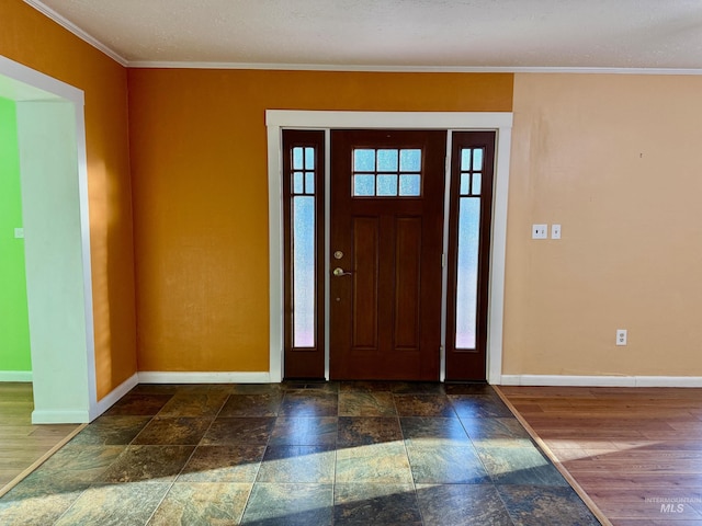 foyer entrance with crown molding, stone finish flooring, and baseboards