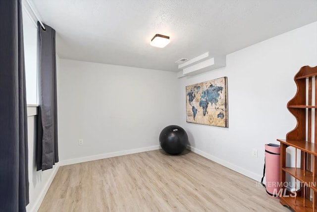 workout area with light wood-type flooring and a textured ceiling