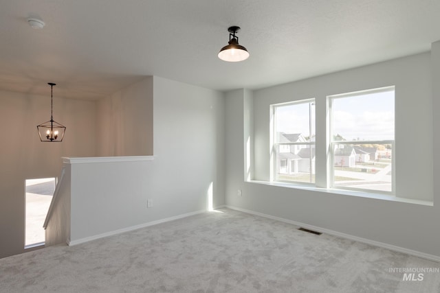 carpeted spare room featuring baseboards, visible vents, and a chandelier