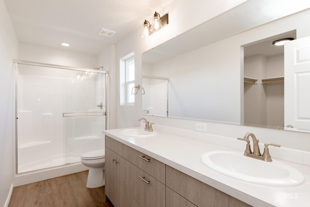 bathroom featuring a sink, wood finished floors, toilet, and a stall shower