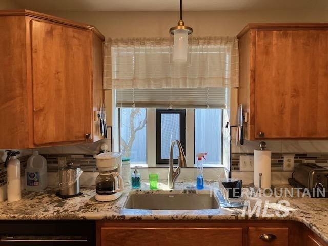 kitchen with pendant lighting, a sink, light stone counters, brown cabinetry, and decorative backsplash