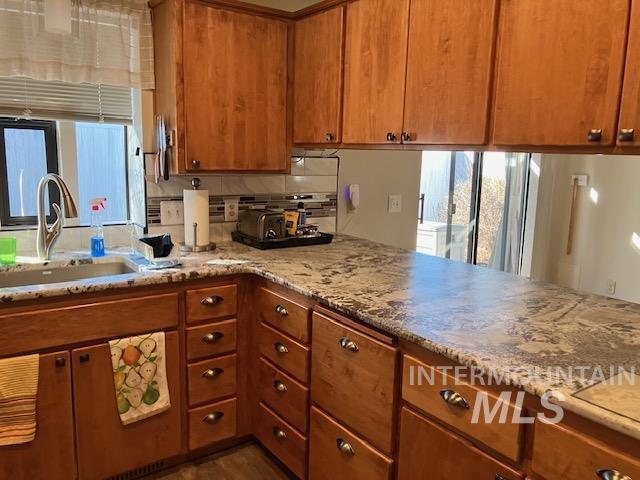 kitchen featuring light stone counters, brown cabinets, backsplash, and a sink