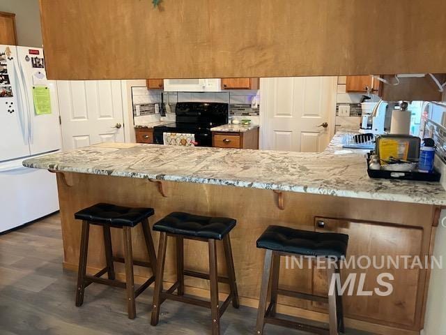 kitchen featuring range hood, a peninsula, freestanding refrigerator, black range with electric cooktop, and brown cabinets