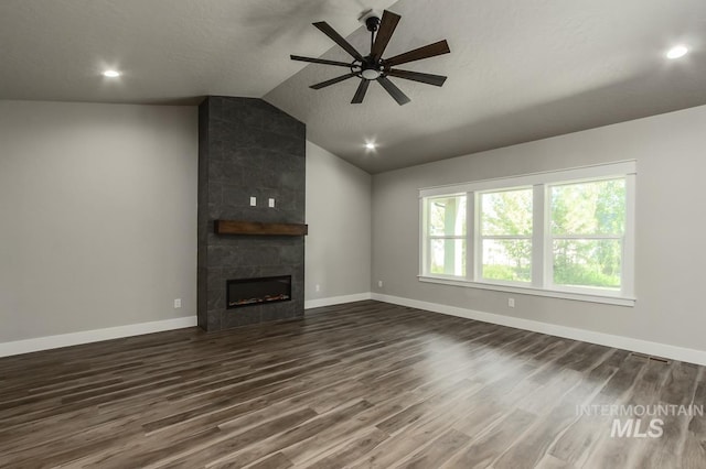 unfurnished living room featuring lofted ceiling, ceiling fan, a tiled fireplace, and dark hardwood / wood-style flooring