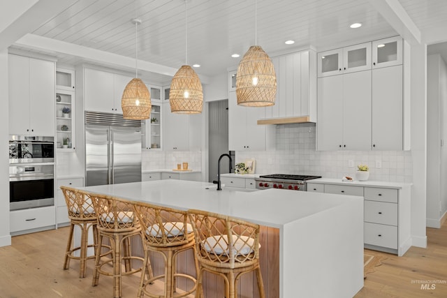 kitchen featuring light wood finished floors, an island with sink, a sink, appliances with stainless steel finishes, and light countertops