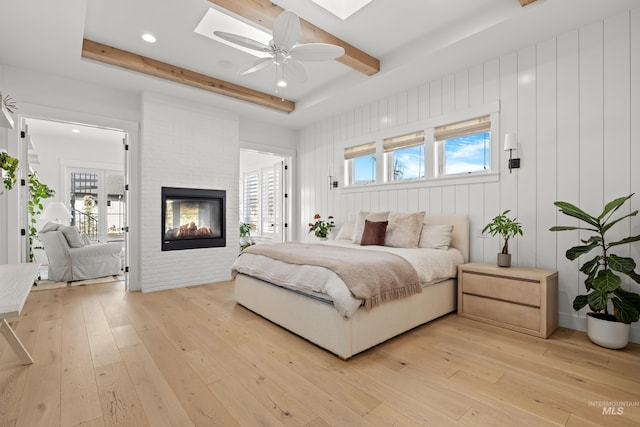 bedroom featuring light wood-type flooring, multiple windows, beamed ceiling, a skylight, and a multi sided fireplace