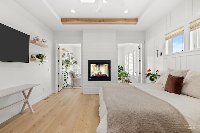 bedroom featuring baseboards, a raised ceiling, light wood-style flooring, and a fireplace