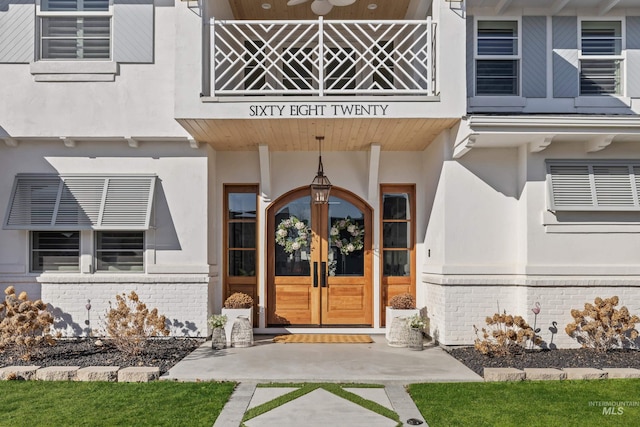 view of exterior entry with french doors, brick siding, a balcony, and stucco siding