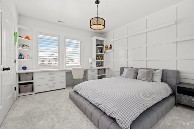 bedroom featuring visible vents, light carpet, built in study area, and a decorative wall