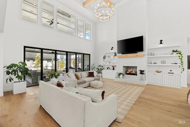 living area featuring a towering ceiling, light wood finished floors, baseboards, a brick fireplace, and a chandelier