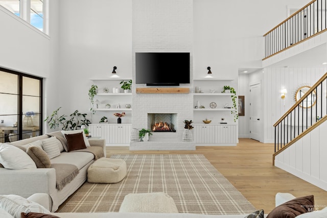 living area featuring stairs, a brick fireplace, a towering ceiling, and light wood finished floors