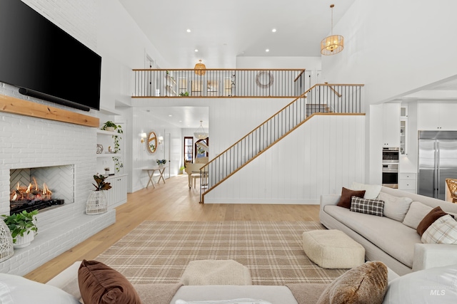 living room with stairway, light wood-style flooring, a high ceiling, recessed lighting, and a brick fireplace