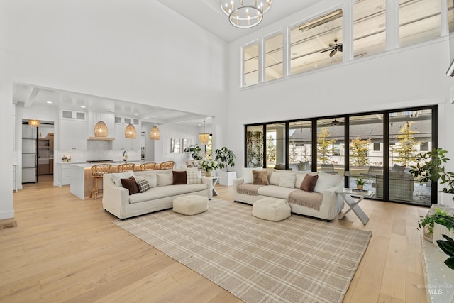 living room with visible vents, light wood-style flooring, ceiling fan with notable chandelier, and a high ceiling