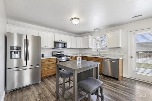kitchen featuring dark wood-style flooring, white cabinets, visible vents, appliances with stainless steel finishes, and a sink